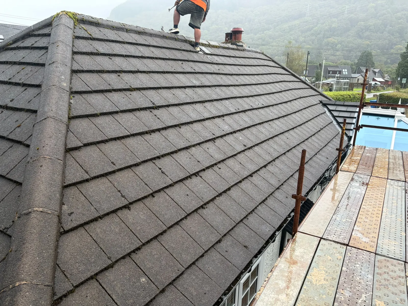 Roofer removing moss from a tiled roof
