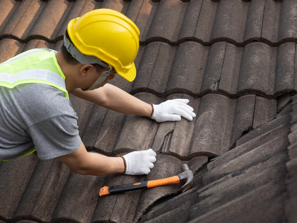 Roofer in a hard hat fixing new concrete tiles to a pitched roof